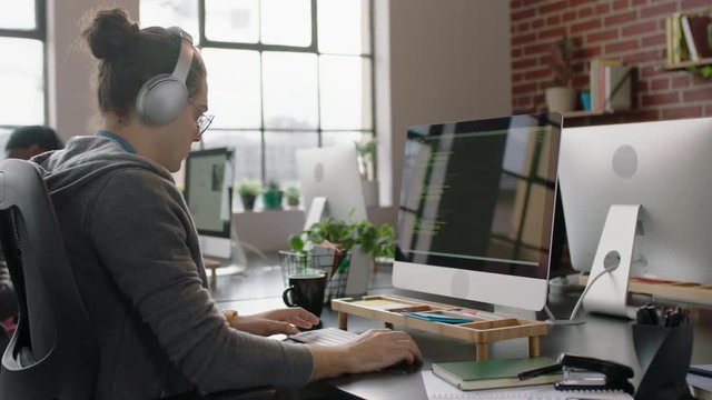 young caucasian man programmer coding network security software for startup company professional web developer typing code on computer screen writing notes listening to music in office 