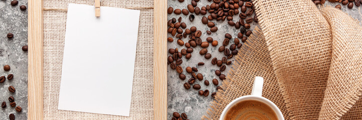 Panoramic photo of a concrete top from above with spilled coffee beans. Wooden frame with mockup, coffee in a white cup and a jute bag