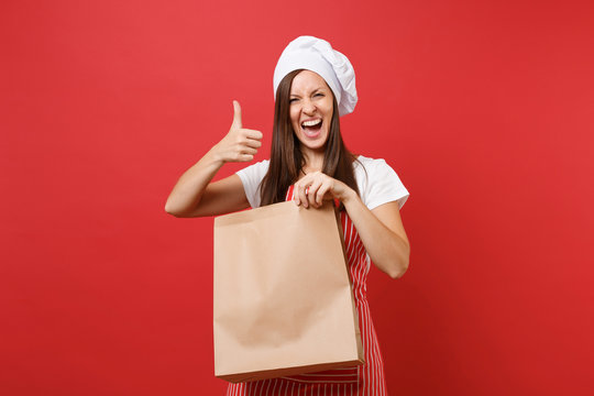 Housewife female chef cook baker in striped apron t-shirt toque chefs hat isolated on red wall background Woman hold in hand brown clear empty blank craft paper bag takeaway Mock up copy space concept
