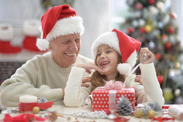 Happy grandfather and child in Santa hats preparing for Christmas