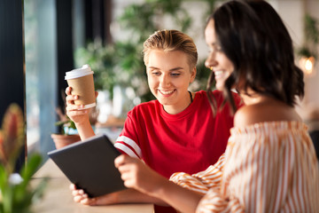 technology and people concept - female friends with tablet pc computer and coffee at cafe