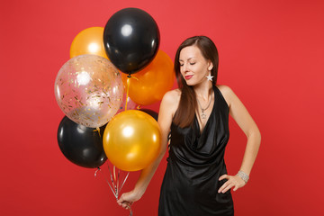 Fototapeta na wymiar Tender young woman in little black dress celebrating holding air balloons isolated on red background. St. Valentine's, International Women's Day, Happy New Year, birthday mockup holiday party concept.