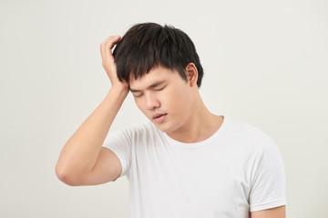 A young man holding his head with his hand looks tired with a headache, isolated on a white background.