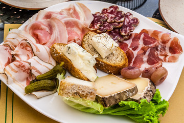 Cold meats and cheeses on a white plate.