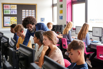 Male Teacher Helping Teenage Female High School Student Working In Computer Class
