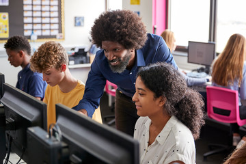 Male Teacher Helping Teenage Female High School Student Working In Computer Class