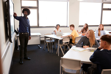 Male High School Teacher Standing Next To Interactive Whiteboard And Teaching Lesson