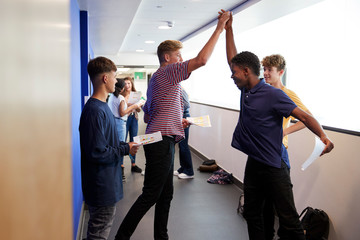 Excited Male Teenage High School Students Celebrating Exam Results In School Corridor