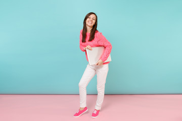 Full length portrait of woman in knitted rose sweater white pants holding laptop pc computer isolated on bright pink blue pastel wall background in studio. Fashion lifestyle concept Mock up copy space