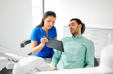Fototapeta premium medicine, dentistry and healthcare concept - female dentist with tablet pc computer and male patient discussing teeth treatment at dental clinic office
