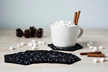 Black fabric coasters and white cup with marshmallows and cinnamon on the table