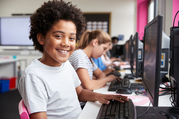 Portrait Of Smiling Male Pupil Sitting In Line Of High School Students Working at Screens In Computer Class - obrazy, fototapety, plakaty