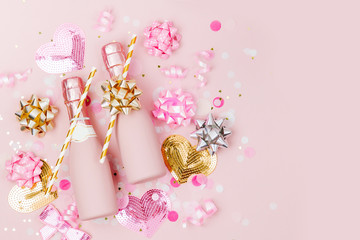 Mini bottles of champagne with confetti and tinsel on Pale Pink background.  Valentines day or birthday party concept theme. Flat lay, top view