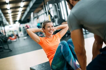 Tuinposter Personal trainer helping young woman reach goals © NDABCREATIVITY