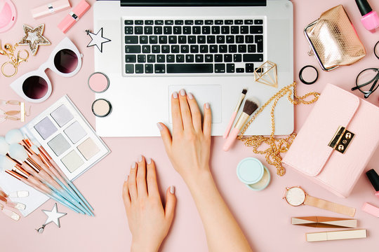 Fashion blogger working with laptop. Workspace with  female accessory, cosmetics products on pale pink table. flat lay, top view