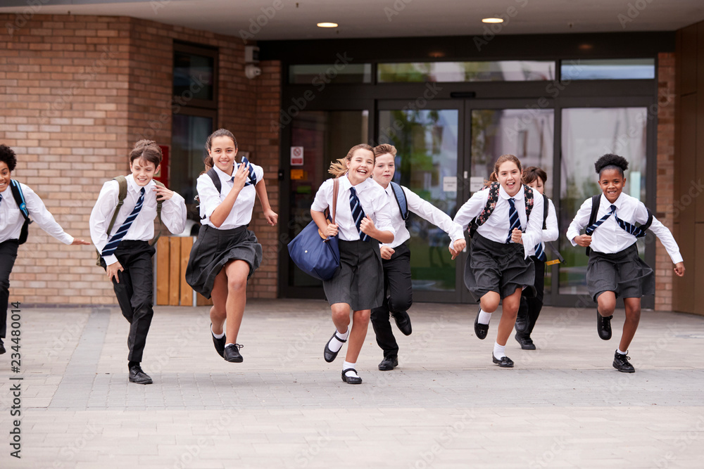 Wall mural Group Of High School Students Wearing Uniform Running Out Of School Buildings Towards Camera At The End Of Class