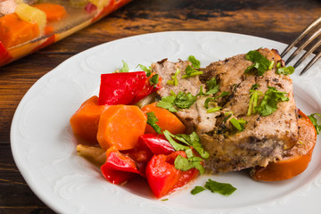 Spicy pork fillet baked with persimmon, apple, onion, carrot, bell pepper and celery on white plate on wooden rustic table