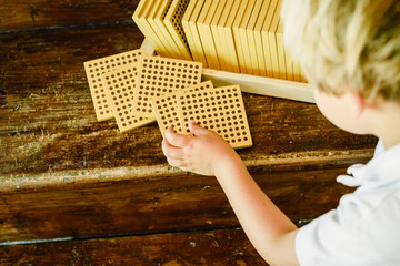 Hands of boy manipulating counting cubes on wooden background in montessori classroom