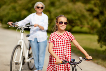 Obraz premium family, leisure and people concept - happy grandmother and granddaughter with bicycles at summer park