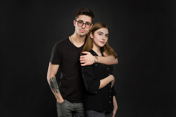 Portrait of young couple in black clothes wearing trendy glasses and posing over black background.