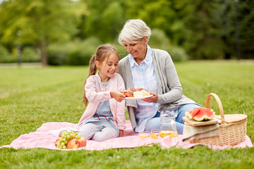 family, leisure and people concept - happy grandmother and granddaughter having picnic at summer park