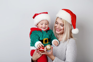 Mother and baby in santa hats with baubles on grey background