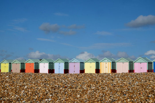 A row of ten colourful Beach huts on Brighton beach the pebble beach in the foreground and a blue sky behind 