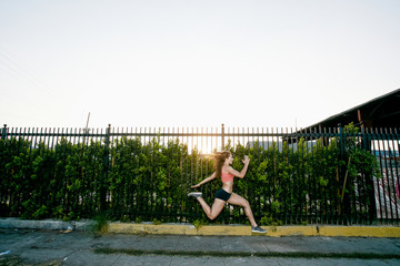 Female athlete running along street at dusk.
