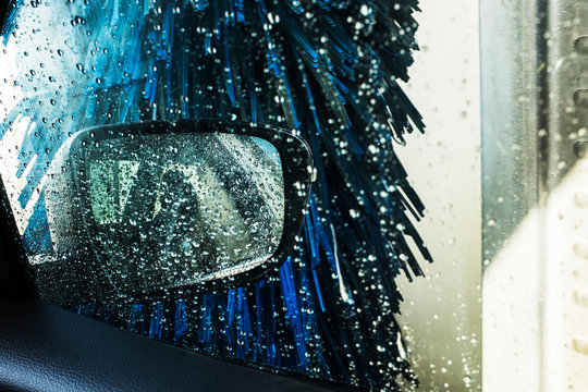 View from the inside of a car in an automated car wash, blue washers and soapy water over the windows.  
