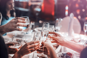 People hold in hands glasses with white wine. wedding party. friends toasting with a champagne above white table