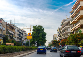 View of the city. Cars moving down the street. On the sides of street are high-rise buildings with spacious balconies. Big crane on the horizon