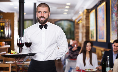 Smiling waiter with serving tray in restaurant