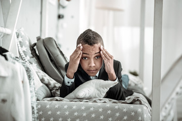So painful. Unhappy young boy holding his temples while having a strong headache