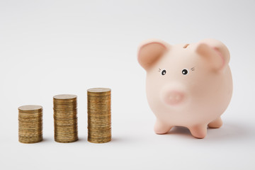 Close up of pink piggy money bank, stacks of golden coins isolated on white wall background. Money accumulation investment banking or business services, wealth concept. Copy space advertising mock up.