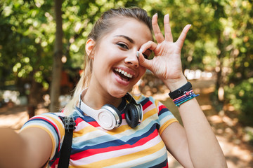 Happy cute young girl take a selfie by camera in park outdoors.