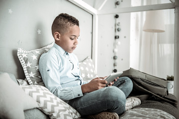 Digital device. Pleasant cute boy playing on his tablet while resting at home