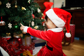 toddler baby girl wearing santa claus costume play in front of christmas tree