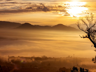 Naklejka premium The village surrounded by mountains at sunrise time with foggy.