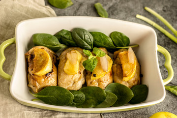 Slices of fried chicken with apples in a baking dish with greens on a dark stone background