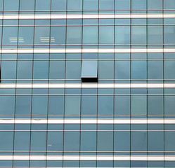 The glass facade of skyscraper with many identical windows and only one window is different. Same glasses structure of house wall with one exception - open window.