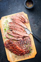 Traditional American barbecue dry aged flank steak sliced as top view on an old board