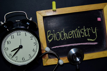 The words Biochemistry handwriting on chalkboard on top view. Alarm clock, stethoscope on black background. With education, medical and health concepts