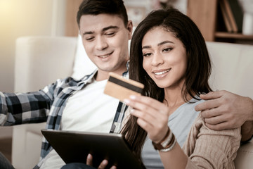 Good mood. Cheerful brunette man embracing his partner and looking at her gadget