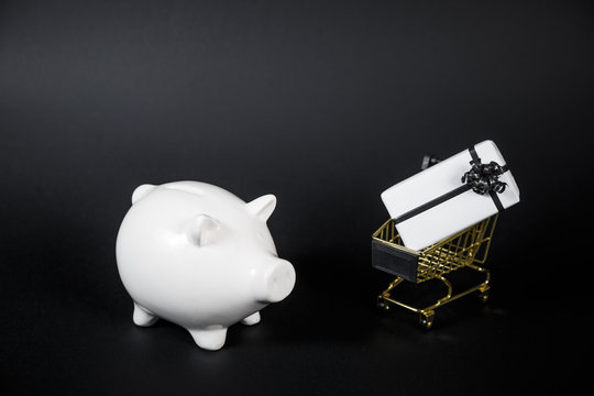 Piggy bank and gift box in shop cart isolated on black background.