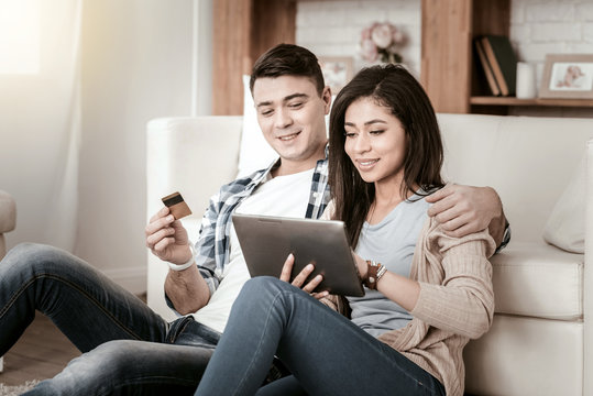 Online shopping. Kind girl expressing positivity while using tablet, sitting near her boyfriend