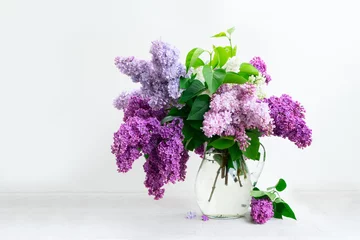 Zelfklevend Fotobehang Verse lila bloemen in glazen vaas op witte tafel achtergrond © neirfy