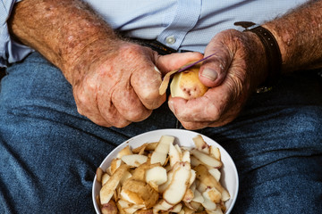 Midsection of man peeling potatoes with knife