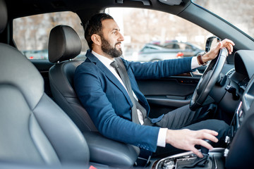 Handsome bearded businessman dressed in the suit driving a car in the city