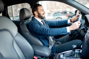 Handsome bearded businessman dressed in the suit driving a car in the city