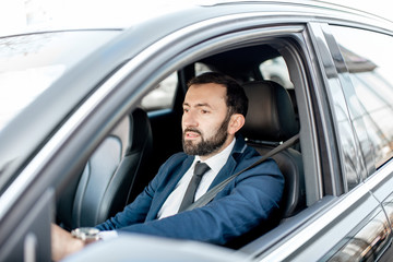 Fototapeta na wymiar Handsome bearded businessman dressed in the suit driving a car in the city